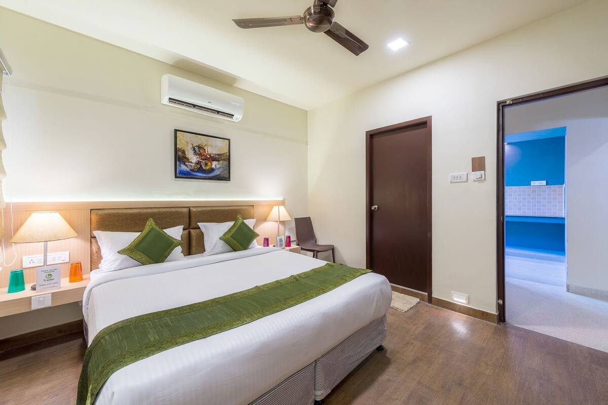 Une chambre d’hôtel comprenant un lit, des lampes de chevet, une table de chevet, un climatiseur, un ventilateur de plafond, une porte et une vue sur la salle de bain.