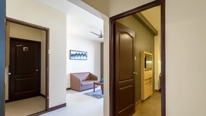 Ein Hotelkorridor mit einer braunen Tür, einer beigen Wand, einem Deckenventilator, einem beigen Sofa und einem kleinen Tisch.