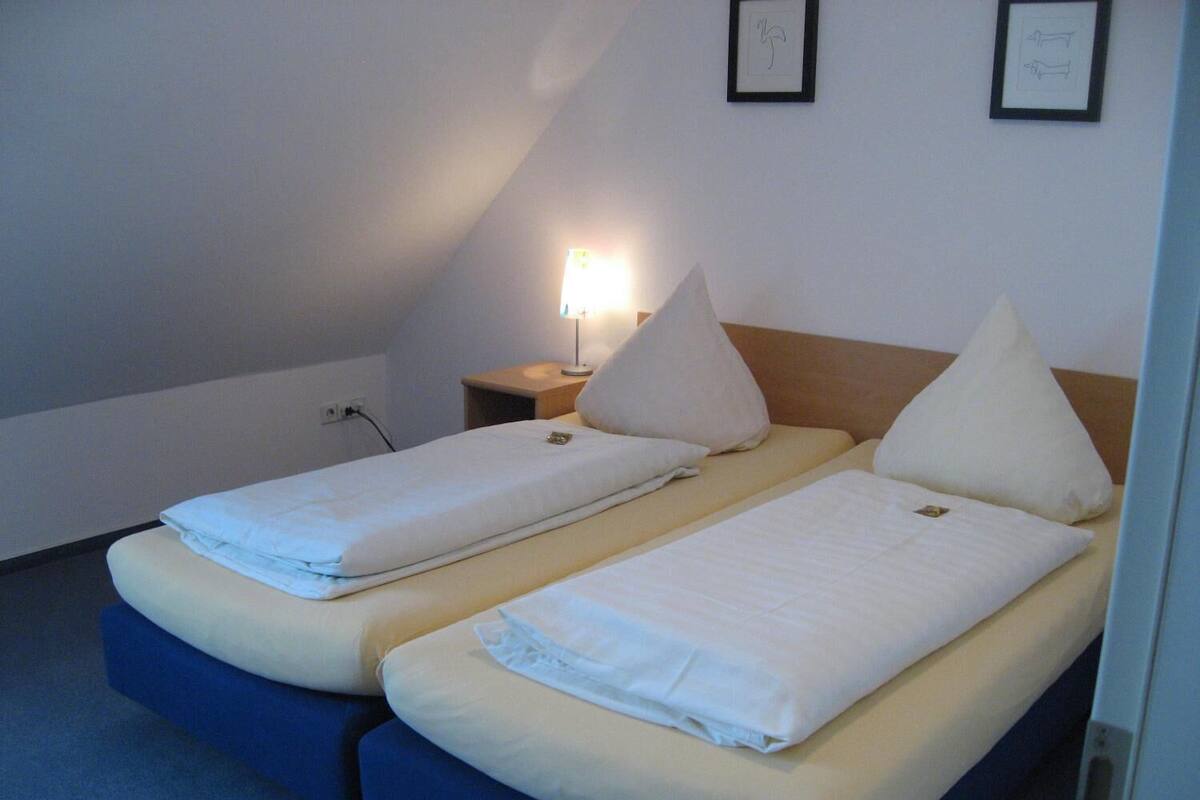 A twin room with two single beds, a bedside table, a lamp, and a framed picture on the wall.