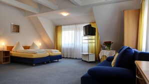 Una camera d'albergo con un letto, un divano, una televisione e un tavolino con un vaso di fiori.