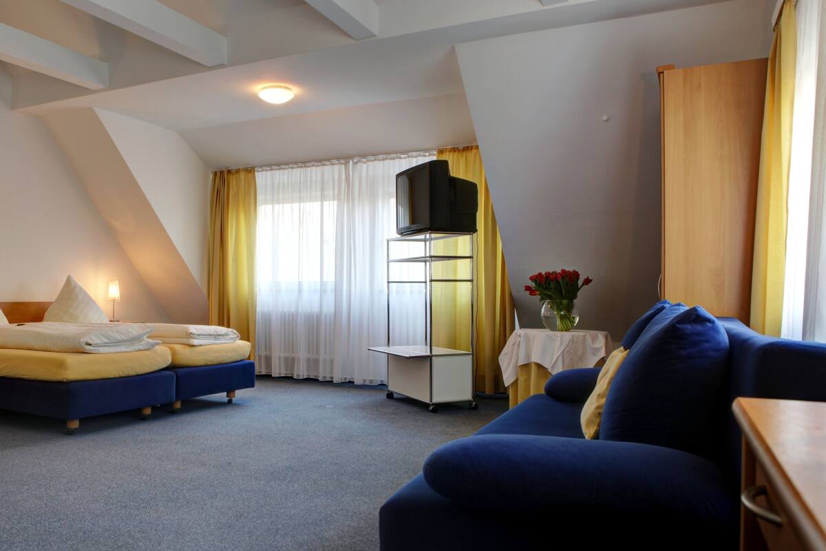 A hotel room with a bed, a sofa, a TV, and a small table with a vase of flowers.