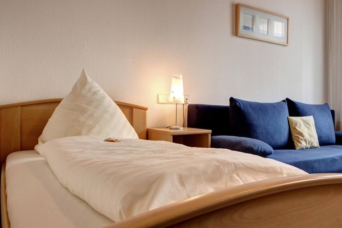 A hotel room with a bed, a bedside table with a lamp, a sofa, and a framed picture on the wall.