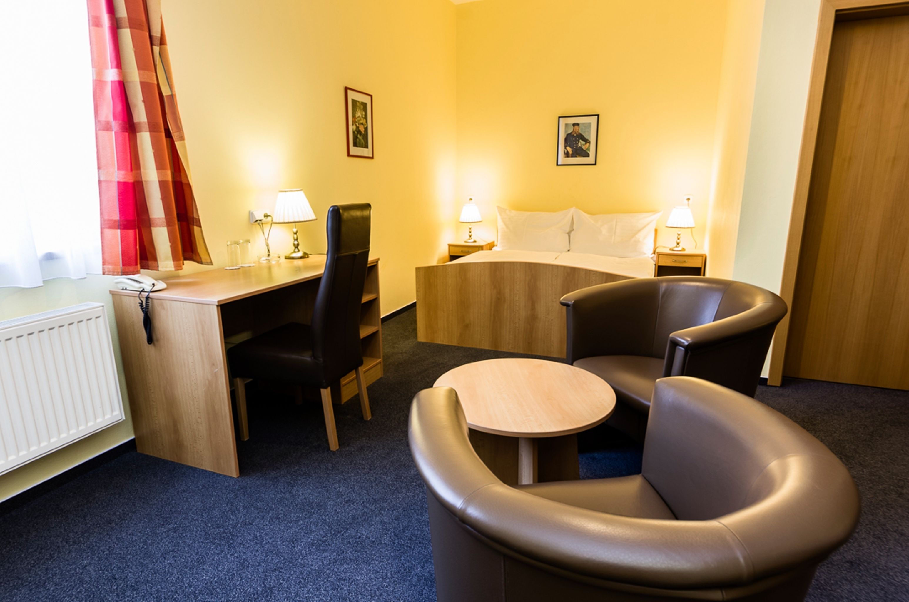 A hotel room with a bed, a desk, a chair, a small table, and two bedside lamps.