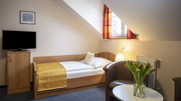 A hotel room with a bed, a TV, a desk, a chair, and a window with curtains.
