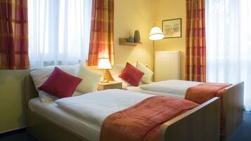 Ein Hotelzimmer mit zwei Betten, einem Nachttisch mit Lampe, einem Regal mit Dekoration und einem Fenster mit Vorhängen.
