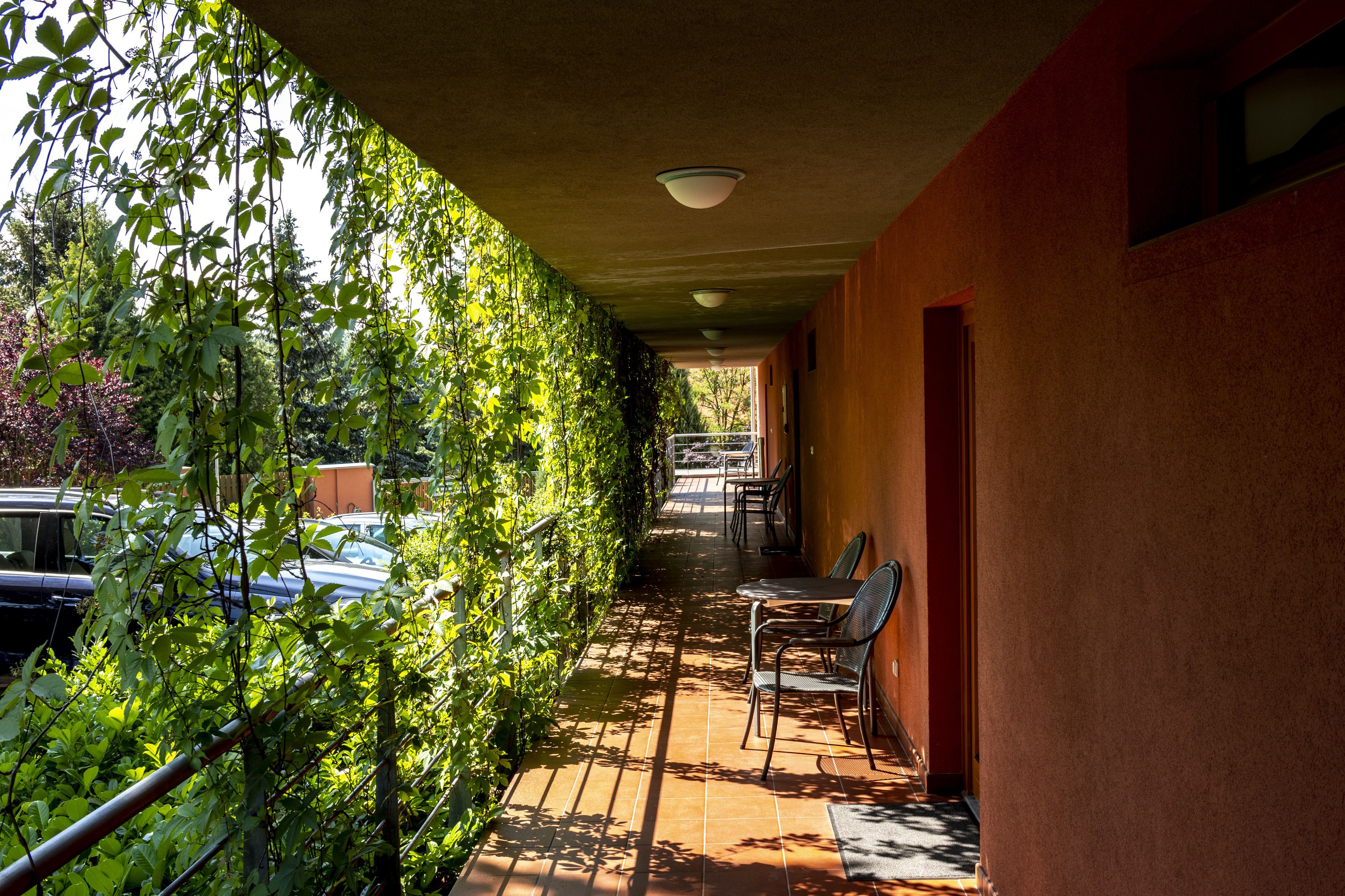 A covered outdoor area with a tiled floor, a metal railing, and a row of chairs.