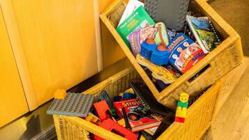 A wicker basket filled with toys and books on a wooden floor.
