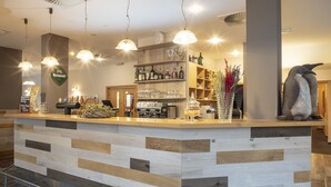 A bar area with a wooden counter, shelves with bottles, and a penguin decoration. - Hotel Pavilon (Ricany)