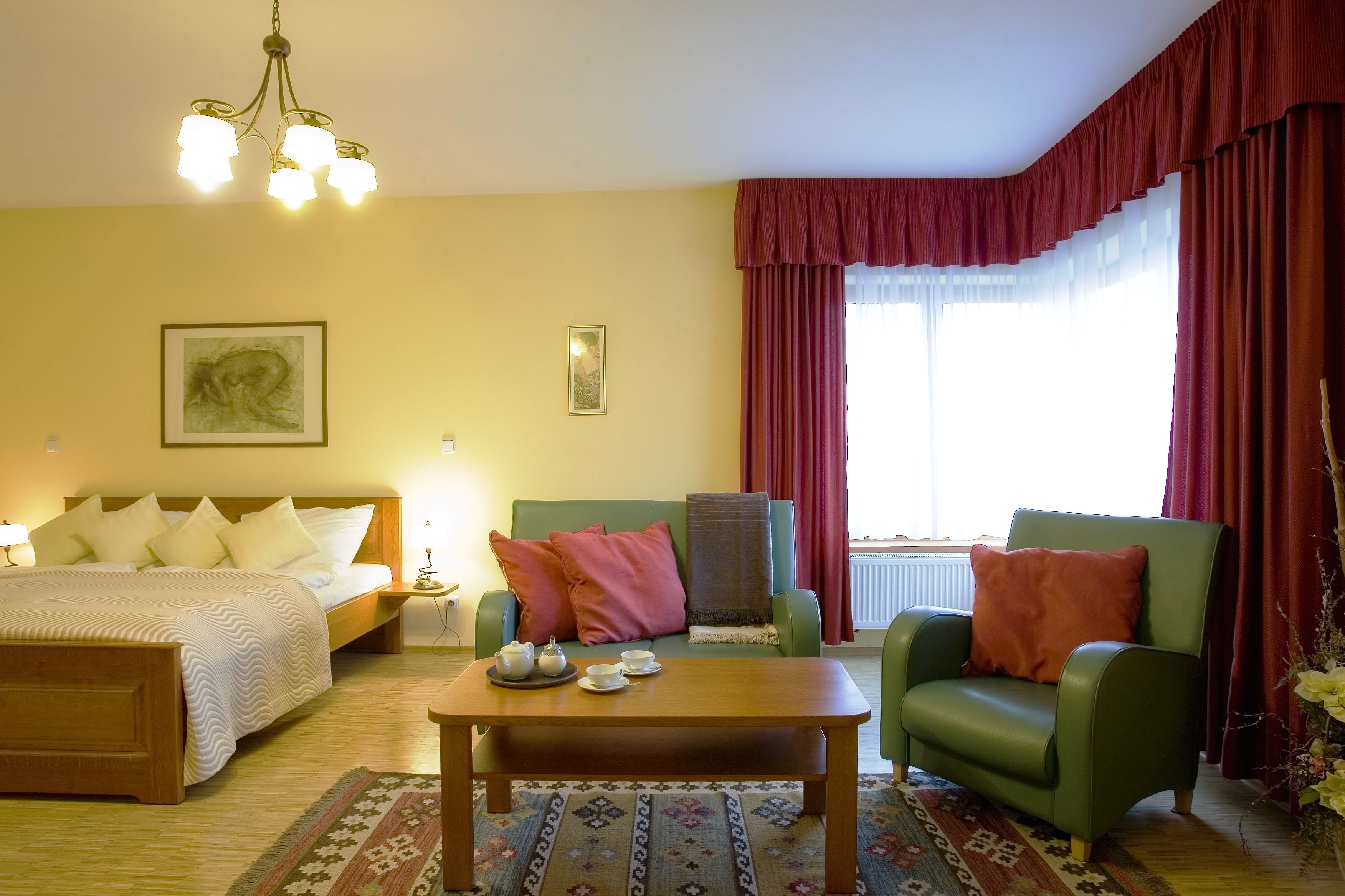 Een hotelkamer met een bed, twee fauteuils, een salontafel en een raam met gordijnen.