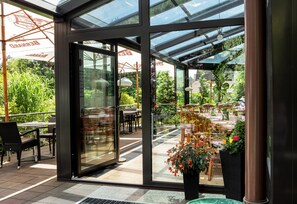 An indoor/outdoor dining area with glass walls, outdoor seating, and potted plants. - Hotel Pavilon (Ricany)