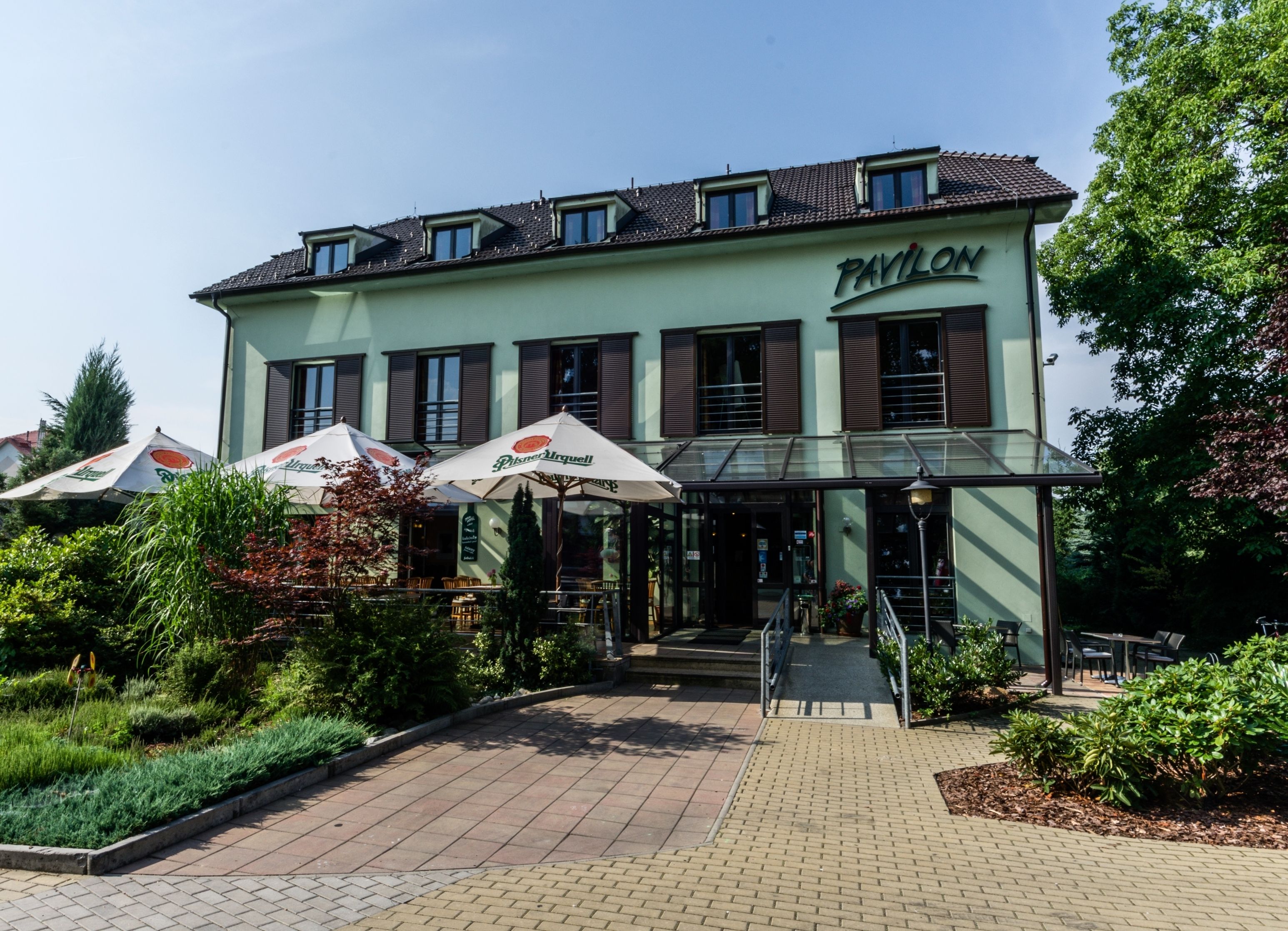 A building with a sign reading "Pavillon" and outdoor seating with umbrellas.