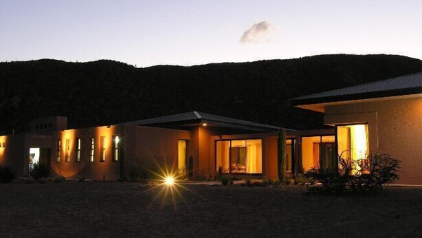 A modern house with a spacious outdoor area, a driveway, and a well-lit entrance. - Chañarmuyo Hotel de Vino (Famatina)