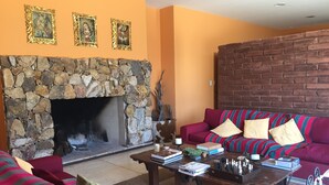 A cozy living room with a stone fireplace, a red sofa, and a coffee table with books and chess pieces. - Chañarmuyo Hotel de Vino (Famatina)