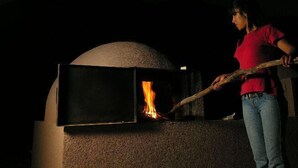 A person using a long-handled tool to manage a fire inside a dome-shaped oven. - Chañarmuyo Hotel de Vino (Famatina)