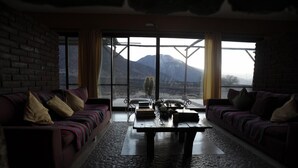 A living room with two sofas, a coffee table, and a view of mountains through large windows. - Chañarmuyo Hotel de Vino (Famatina)