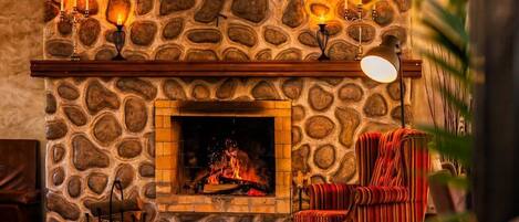 A stone fireplace with a clock above it, a lit candelabra, and a striped armchair.