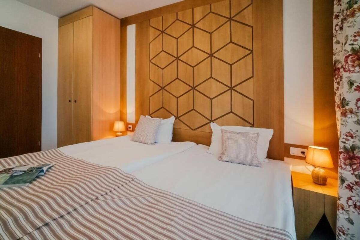 A hotel room with two beds, a wooden headboard with a geometric pattern, and a floral curtain.