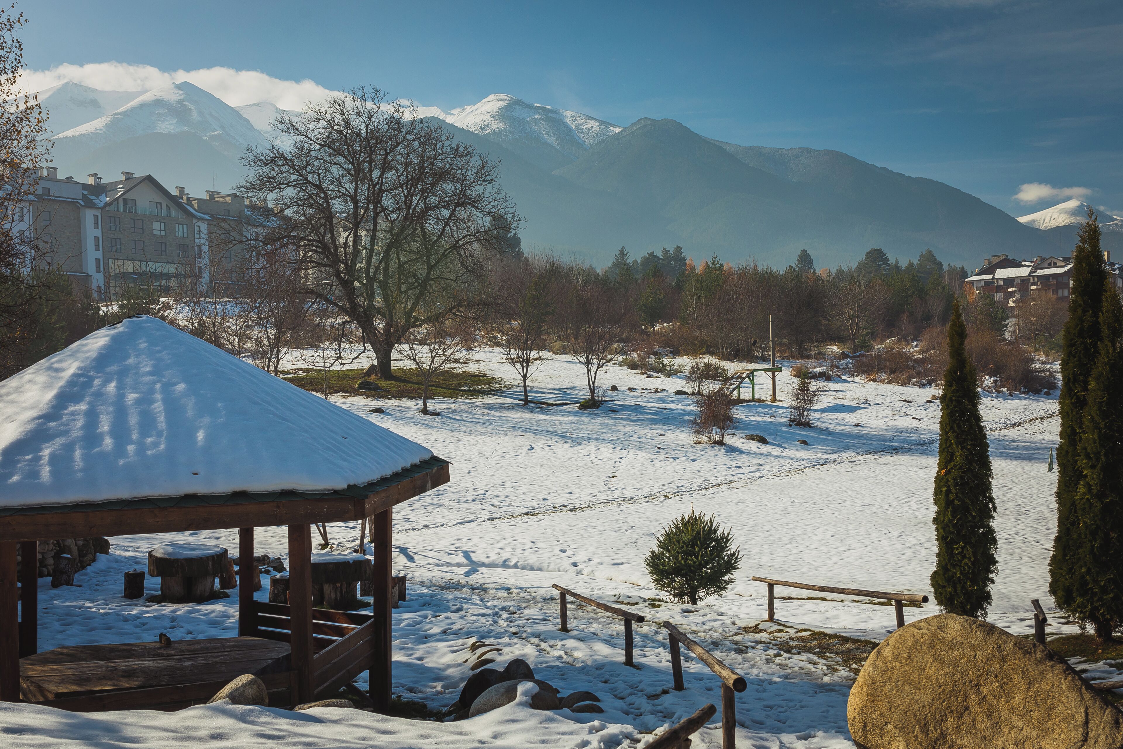 A snow-covered outdoor area with a wooden gazebo, a bench, and a hay bale.