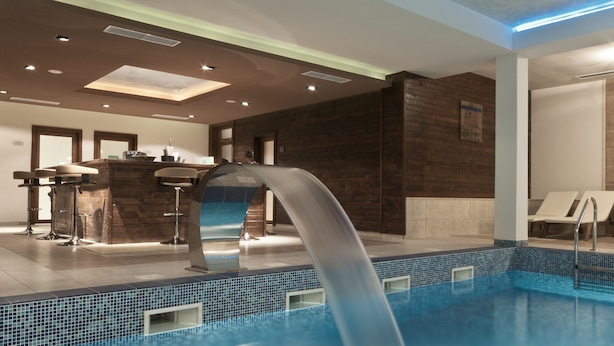 Ein moderner, überdachter Poolbereich mit Wasserfall, Bar und Lounge-Möbeln.