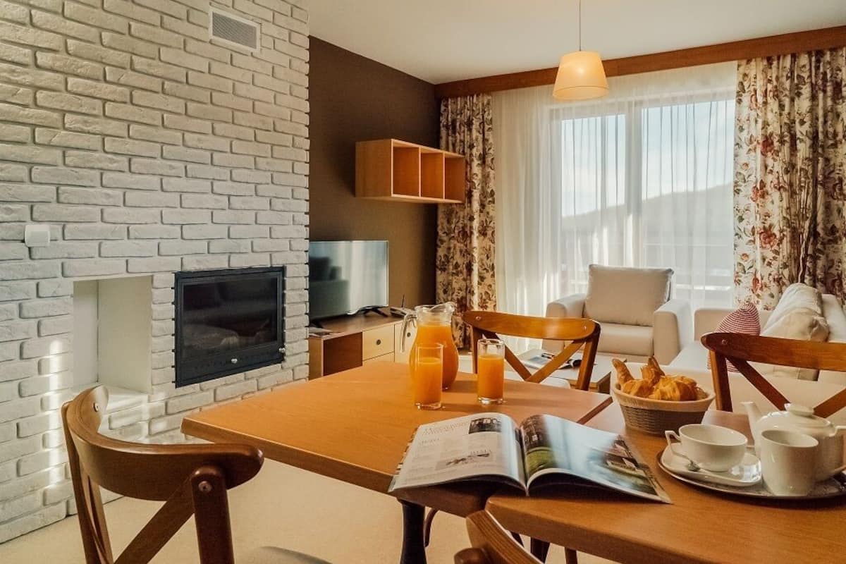 A cozy living room with a brick wall, a fireplace, a television, and a dining area with breakfast items.