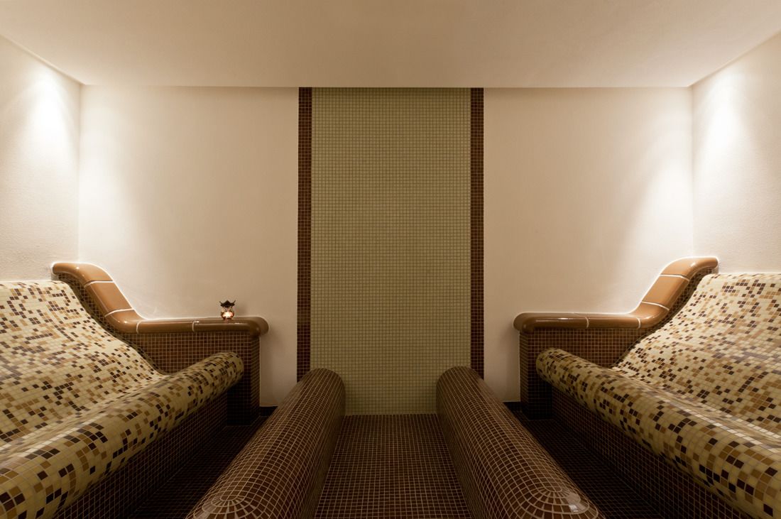 Une salle de spa dotée de deux coins salon avec des sièges rembourrés, d’un mur carrelé et d’un petit objet décoratif accroché au mur.