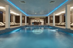 An indoor swimming pool with a tiled floor, lounge chairs, and a bar area. - Green Life Bansko (Bansko)