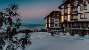 Ein mehrstöckiges Hotel mit Balkonen und großen Fenstern, umgeben von verschneiter Landschaft und Palmen.