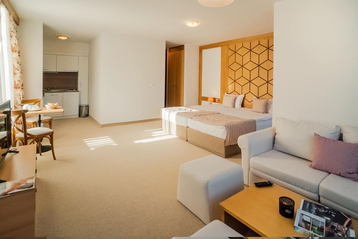 A modern hotel room with a bed, sofa, and a small kitchenette.