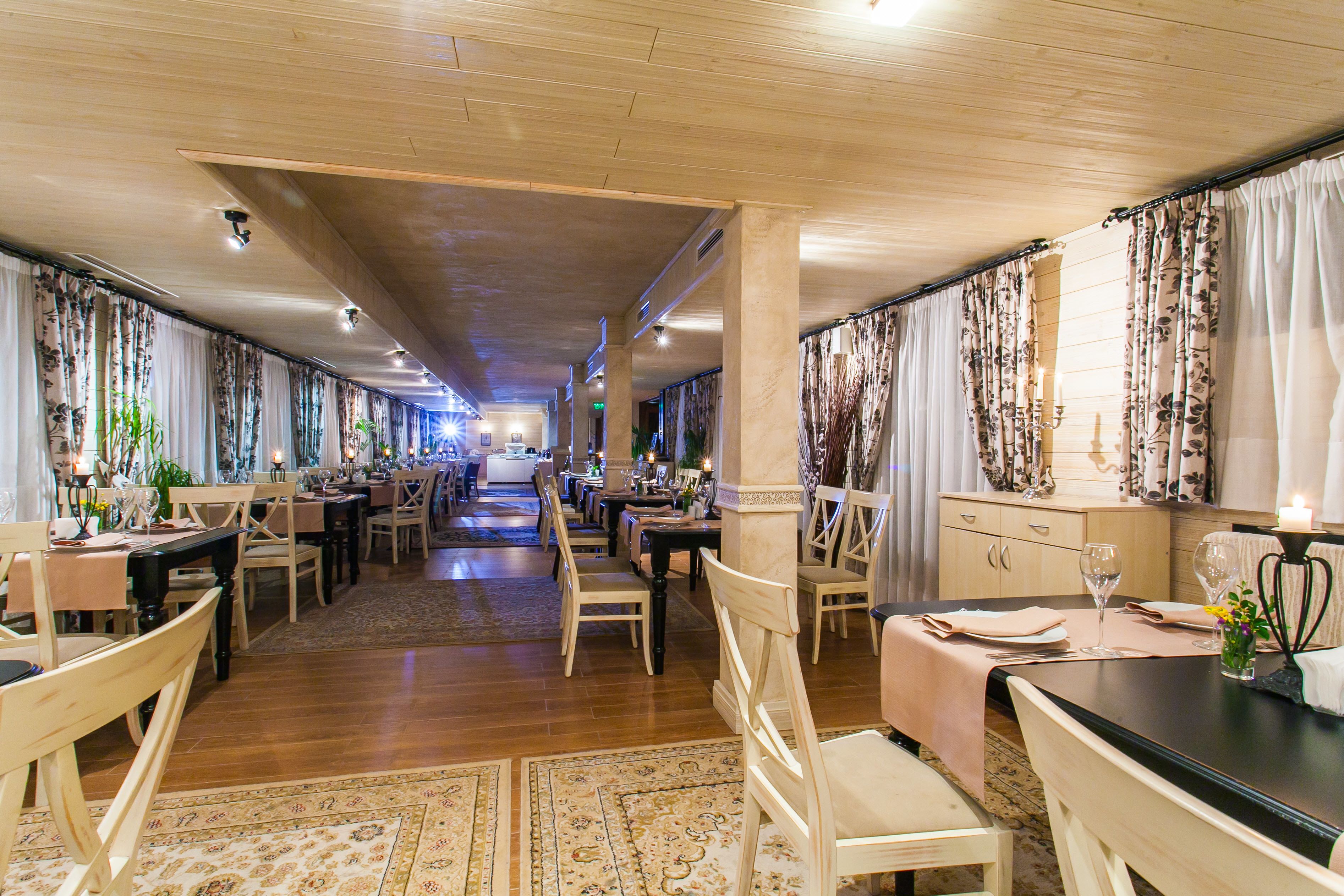 A spacious hotel dining area with wooden floors, multiple dining tables, and chairs.