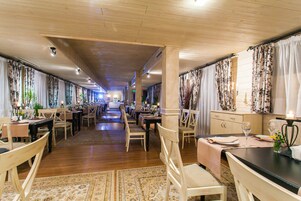 A spacious hotel dining area with wooden floors, multiple dining tables, and chairs.