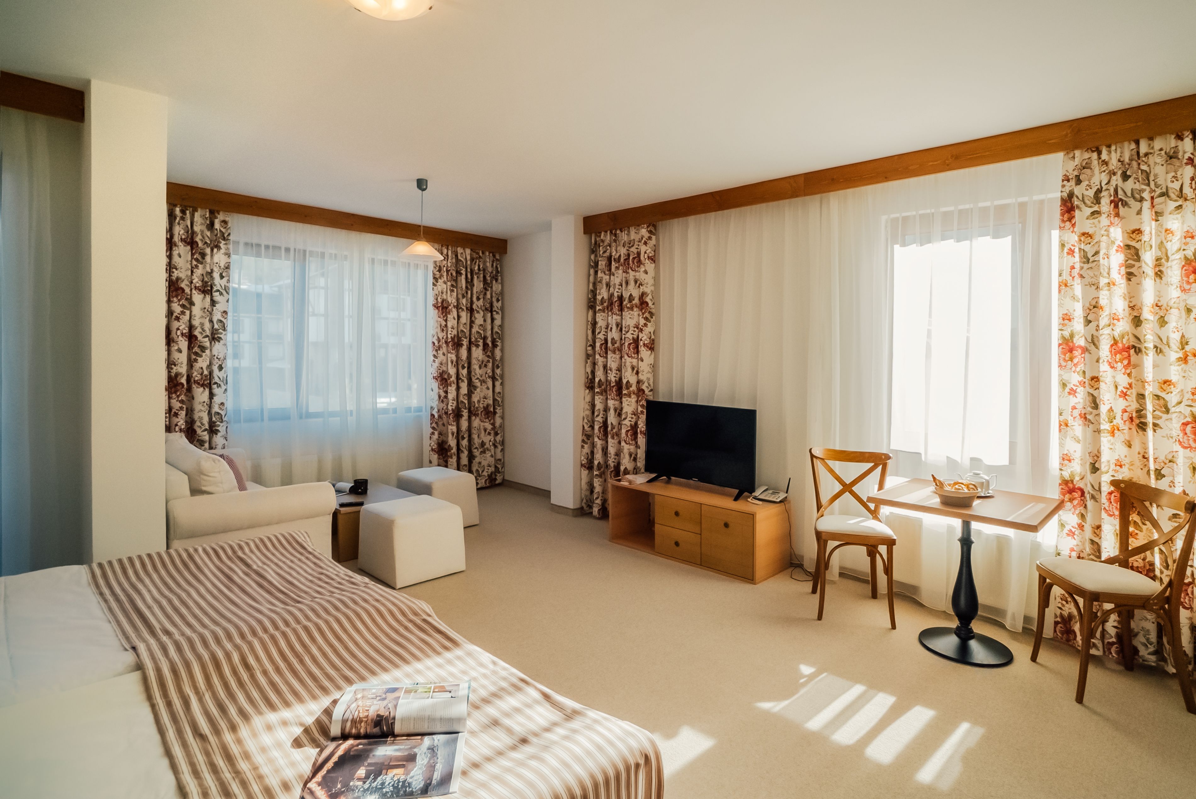 A hotel room with a large bed, a TV, a small table with chairs, and a sofa.