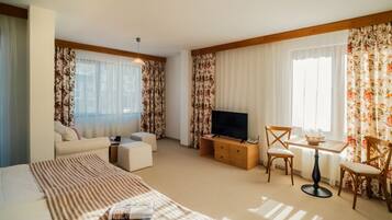 A hotel room with a large bed, a TV, a small table with chairs, and a sofa.