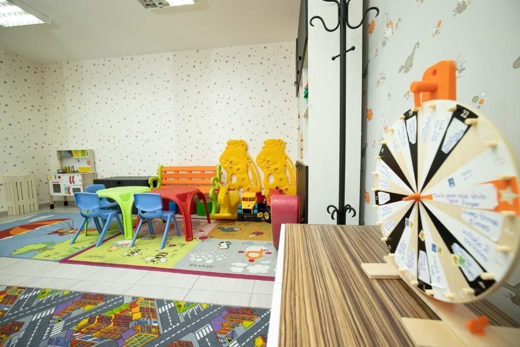 Un salón infantil con tapetes de juego coloridos, una mesa de madera y un dardo.
