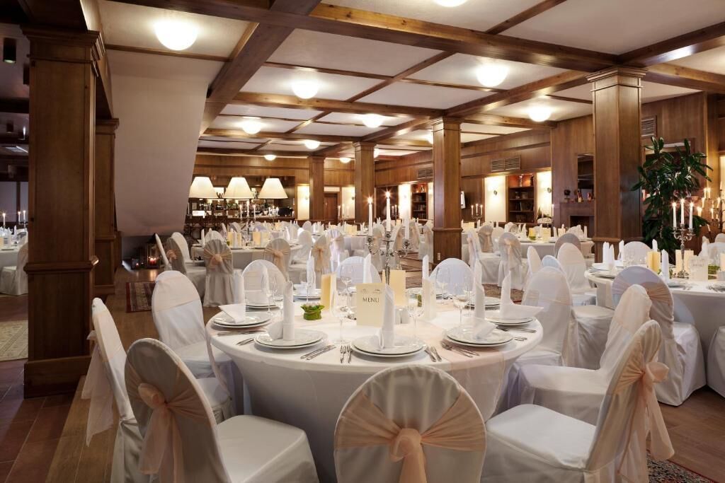 A banquet hall with round tables set for a formal event, featuring white tablecloths, chairs with sashes, and candle centerpieces.