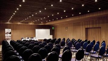 A conference room with rows of chairs facing a presentation screen, wooden paneling on the walls, and a ceiling with evenly spaced lights.