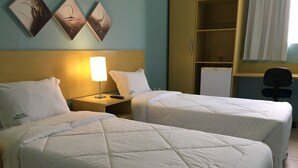 Dos camas individuales con ropa de cama blanca, una mesita de noche con lámpara y un escritorio pequeño con silla.