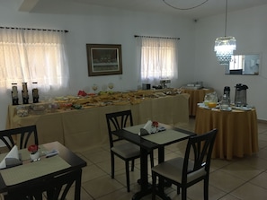 Un comedor con mesas preparadas para el desayuno, una barra de buffet y una estación de café.