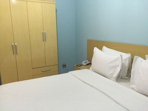 Una habitación de hotel con una cama, almohadas blancas, un armario de madera y un teléfono junto a la cama.
