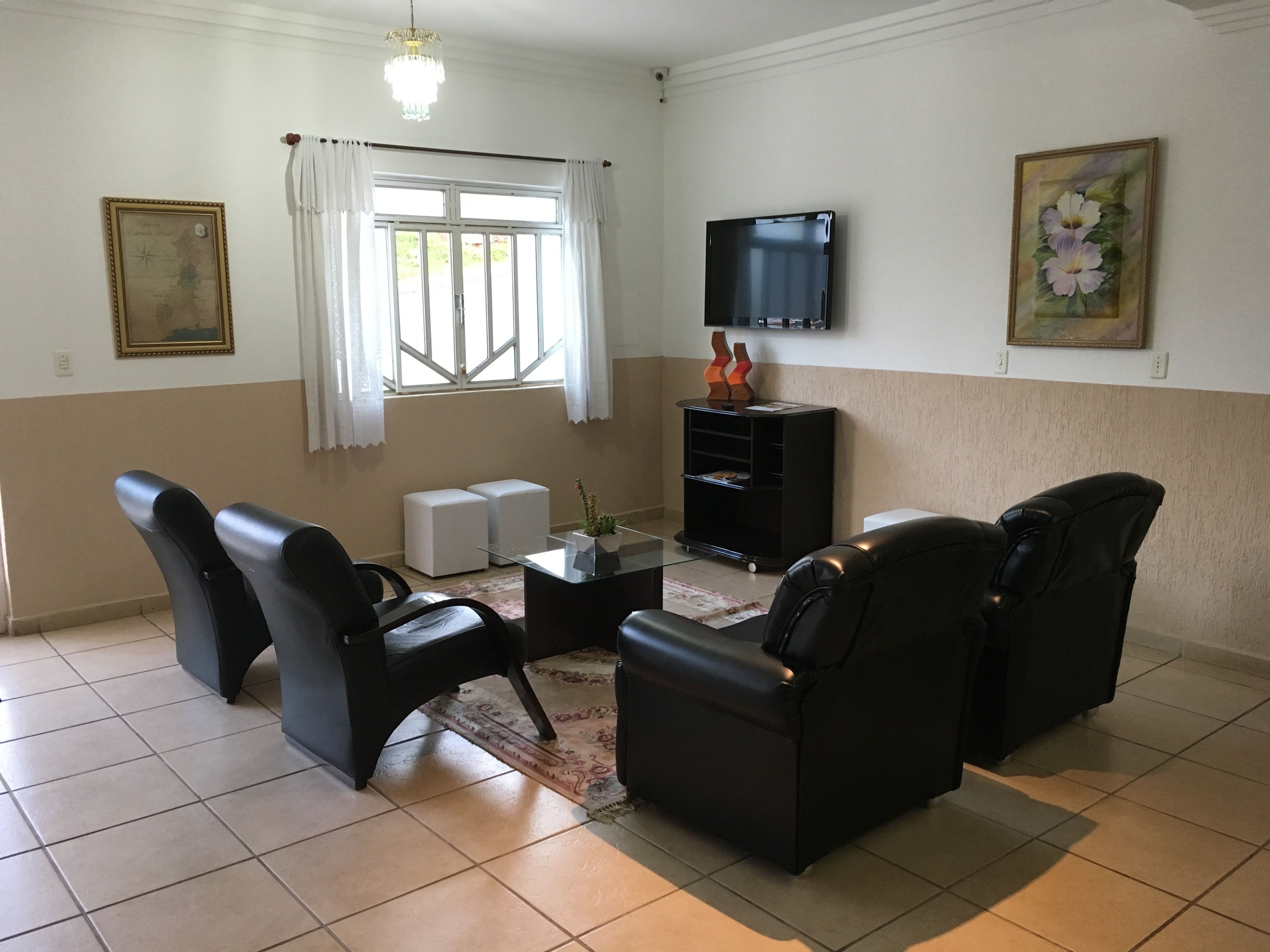 Sala de estar com televisão de tela plana, dois sofás de couro preto, mesa de centro e um pequeno armário branco.