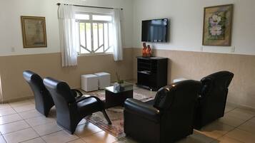 Sala de estar com televisão de tela plana, dois sofás de couro preto, mesa de centro e um pequeno armário branco.