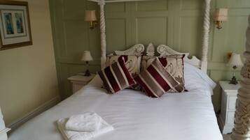 A four-poster bed with white bedding and striped pillows, a white nightstand with a lamp, and a framed picture on the wall.