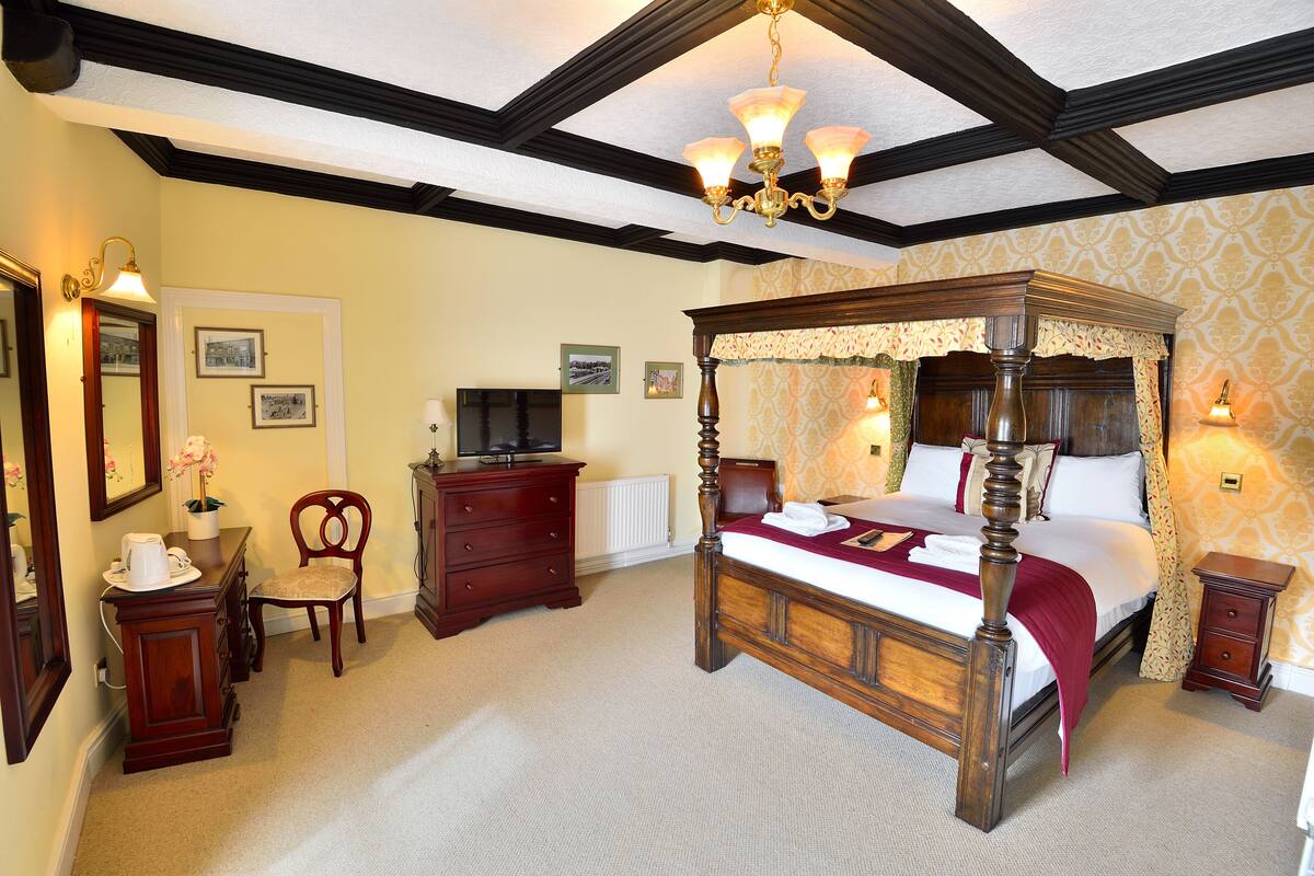 A traditional four-poster bed with a canopy, a wooden dresser, a chair, and a television on a stand.
