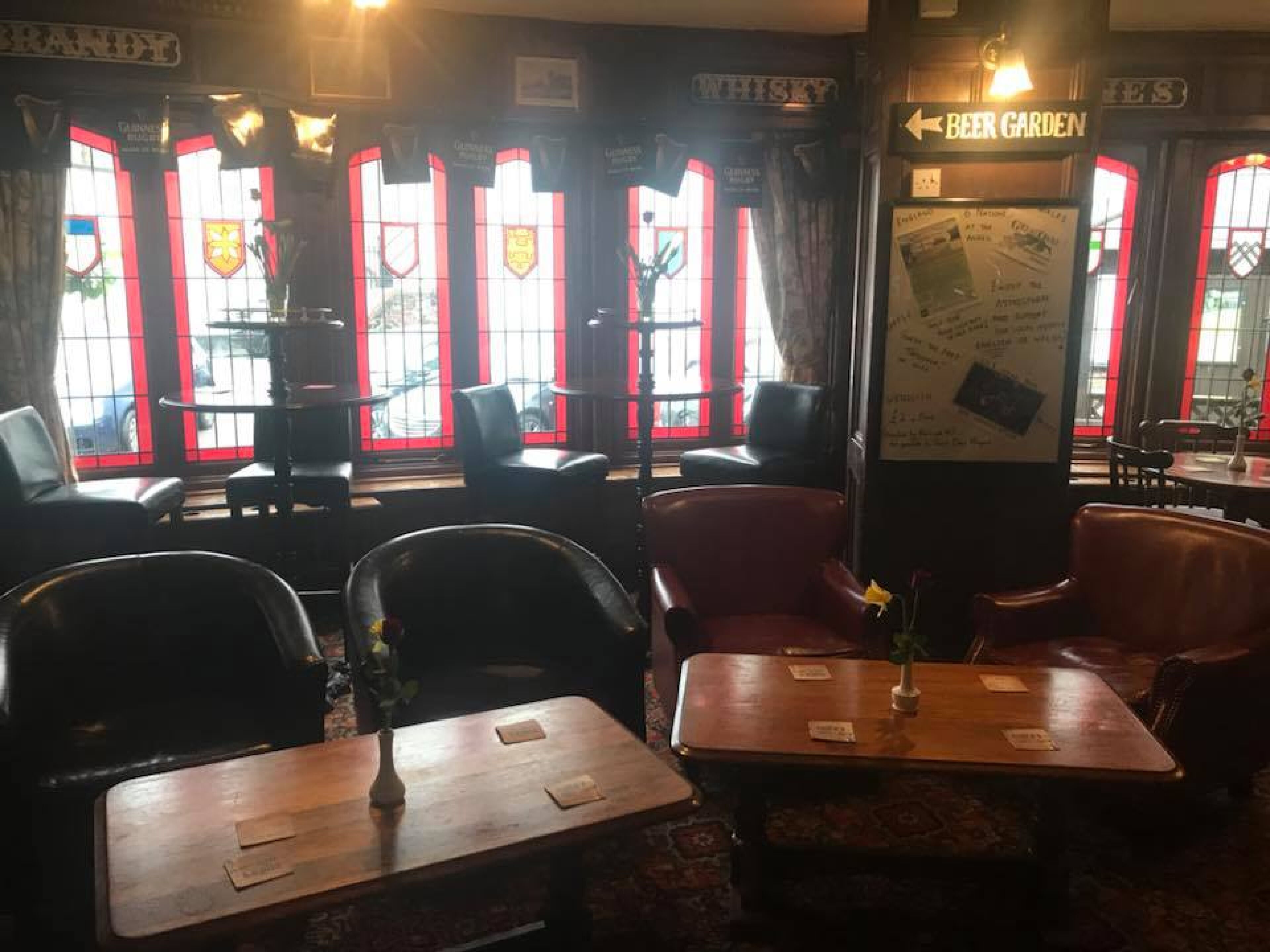 Interior de un pub con ventanas de marco rojo, asientos de cuero y un cartel que indica el jardín de cerveza.