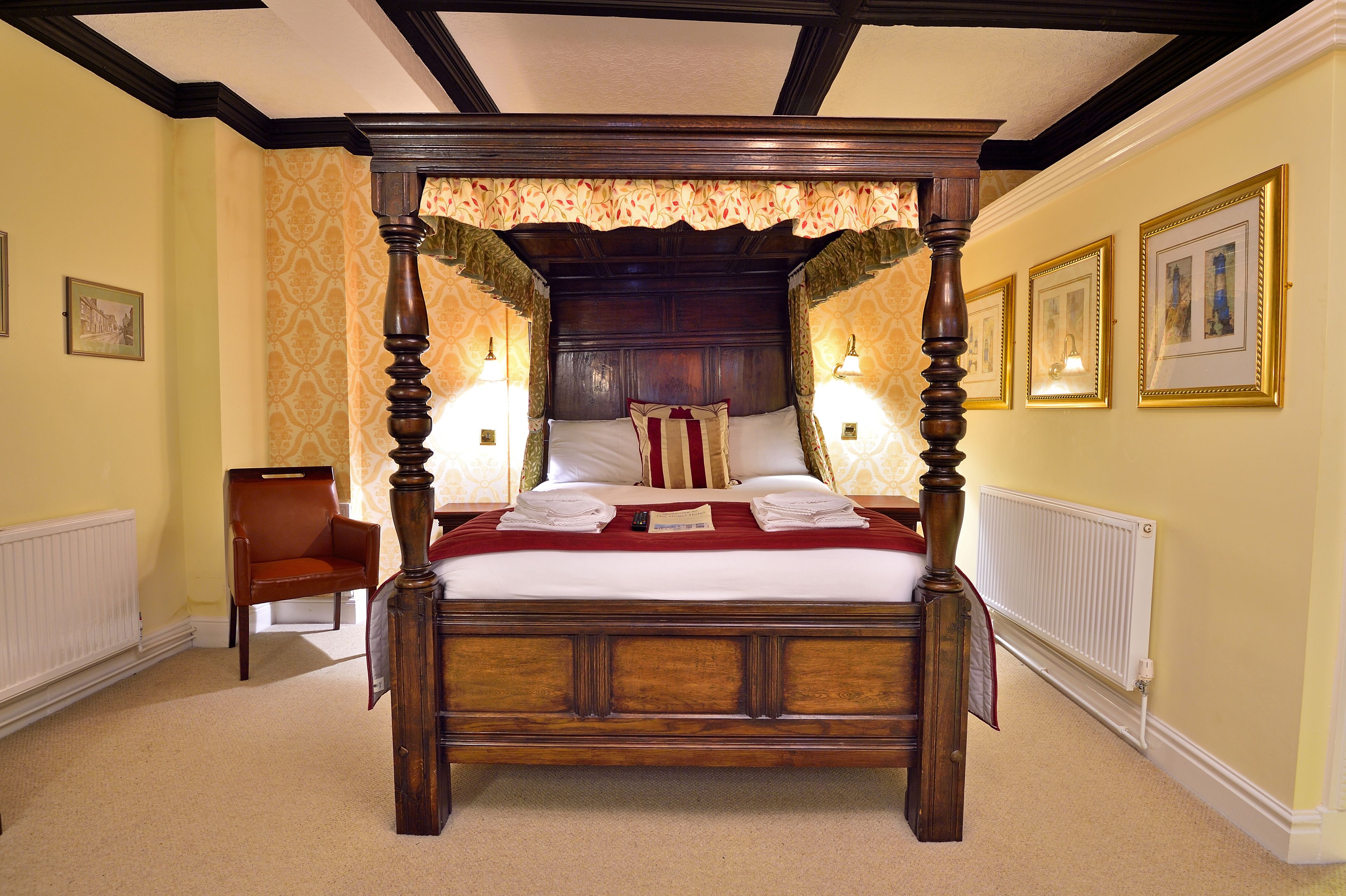 A four-poster bed with a canopy, a chair, and framed pictures on the walls.