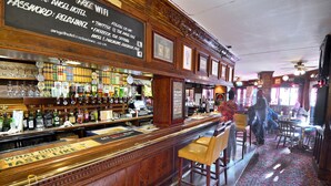 A bar area with a wooden counter, various bottles, glasses, and a signboard with social media information. - The Angel Hotel (Coleford)
