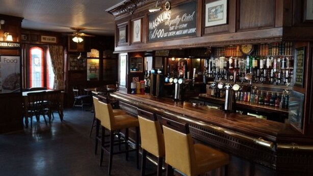A bar with wooden bar tops, multiple stools, and a variety of bottles and glasses. - The Angel Hotel (Coleford)