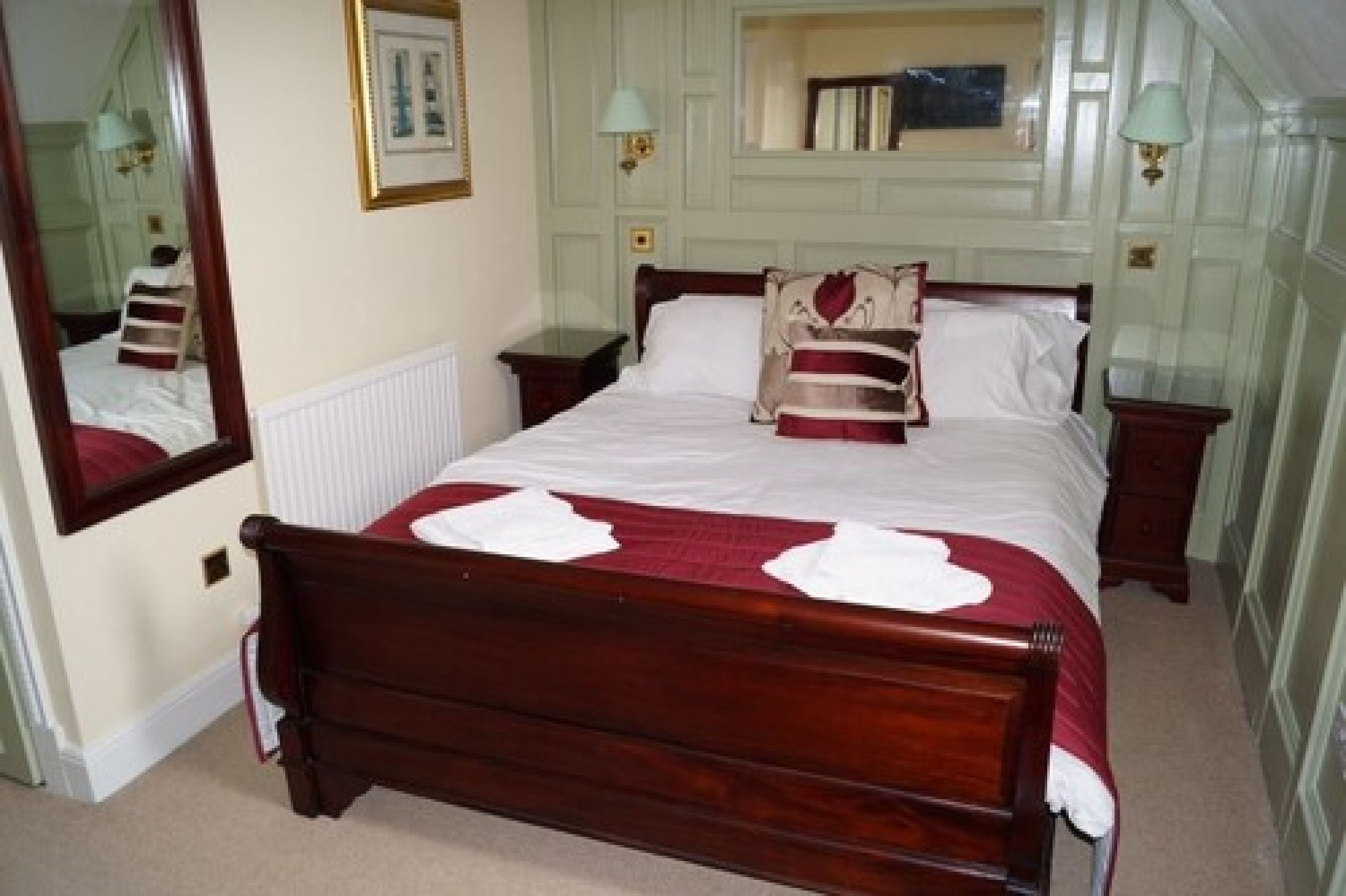 A neatly made bed with a wooden frame, a mirror, and two bedside tables with lamps.