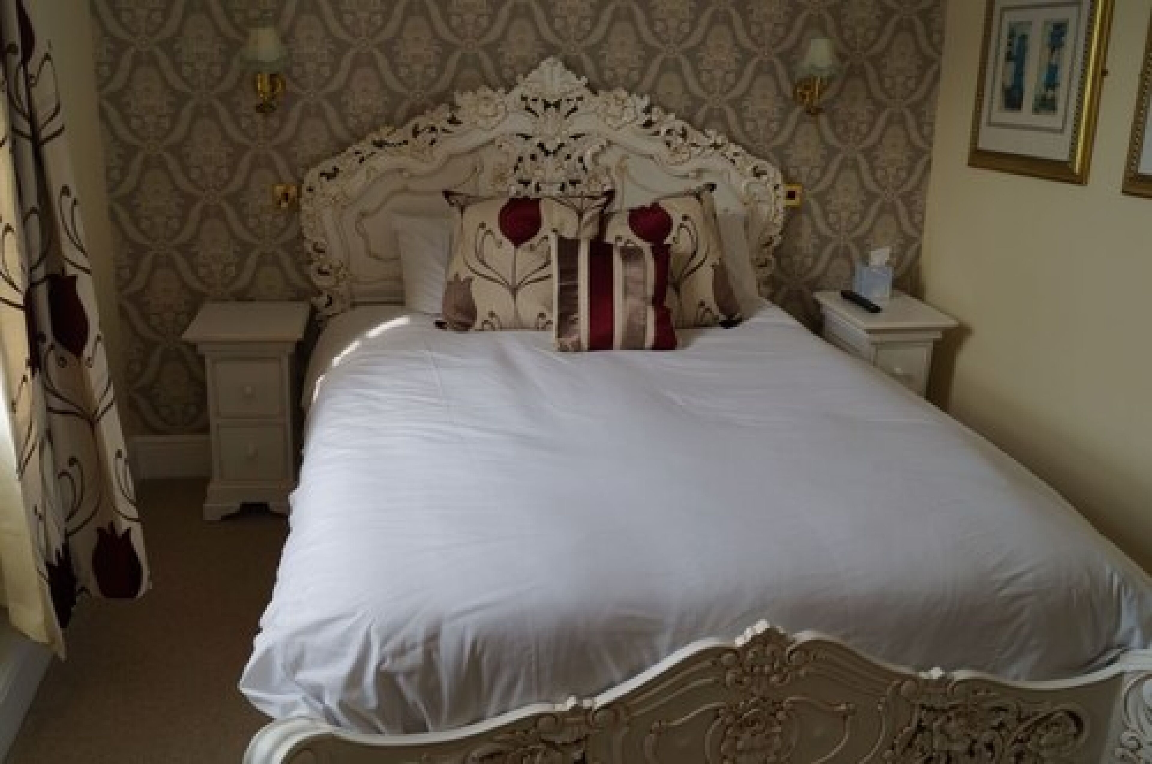 A bedroom with a large bed, ornate headboard, and two bedside tables.