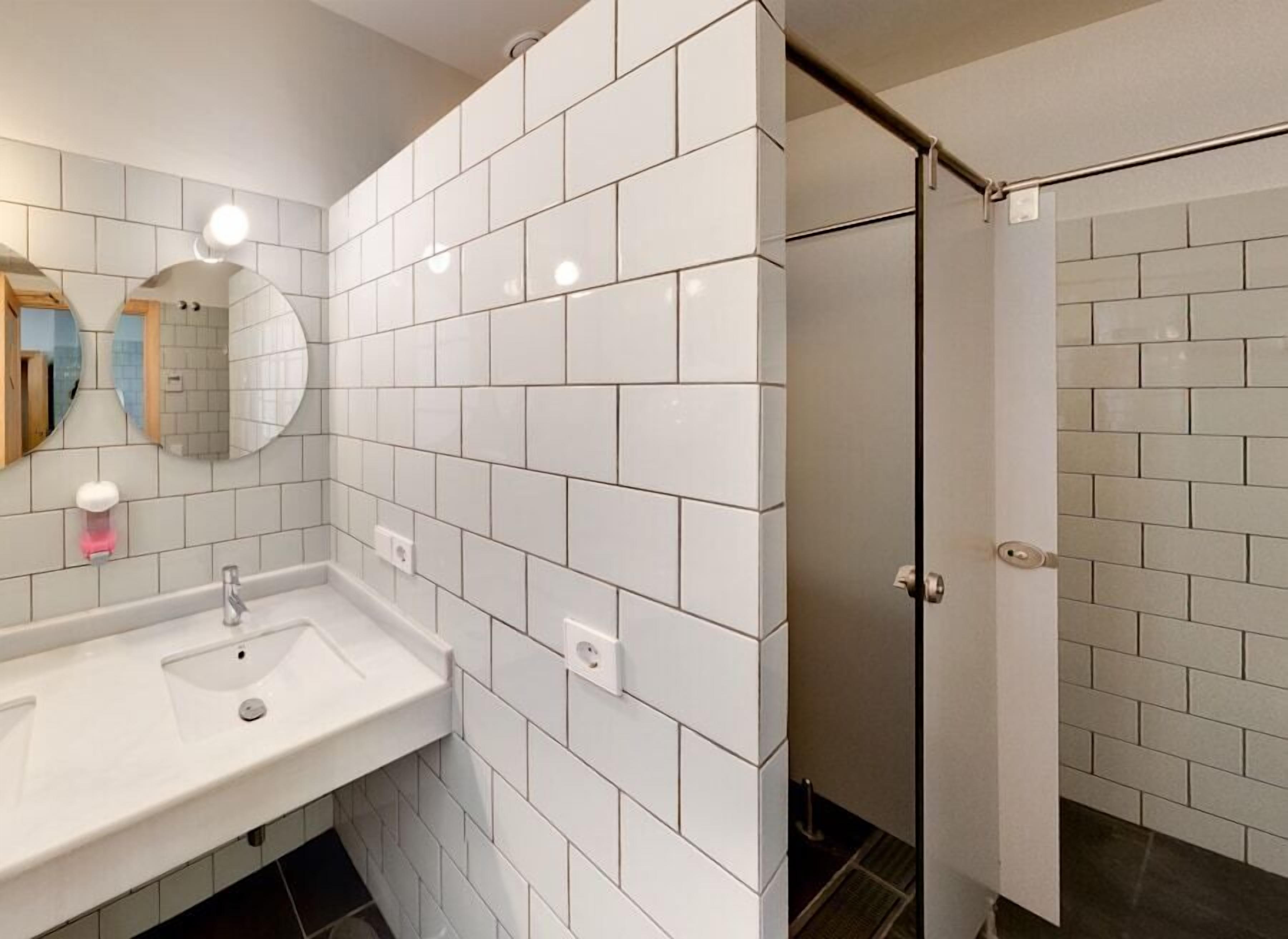 A modern bathroom with white subway tiles, a sink with a mirror, and a shower area.