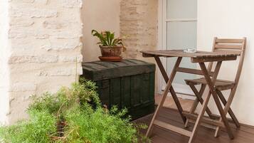 A small outdoor seating area with a wooden table and chairs, a potted plant, and a wooden planter with greenery.